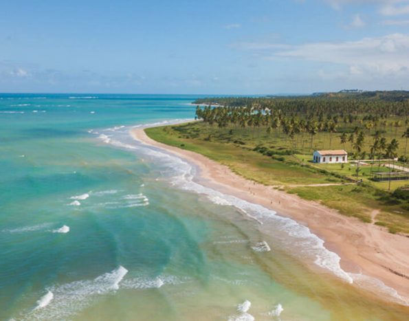 foto aérea da praia de são miguel dos milagres com o mar turquesa e a igreja de longe