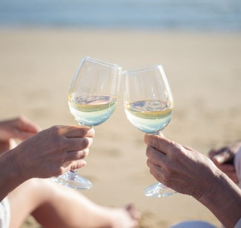 casal na praia com taças de vinho branco, representando onde comemorar aniversário de casamento