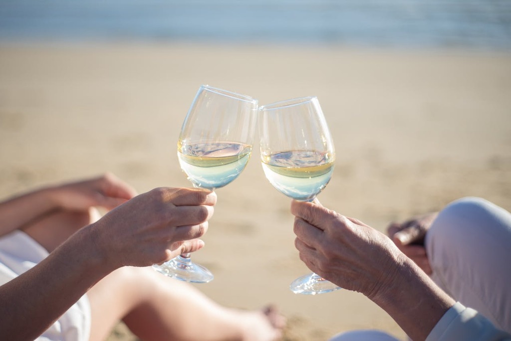casal na praia com taças de vinho branco, representando onde comemorar aniversário de casamento