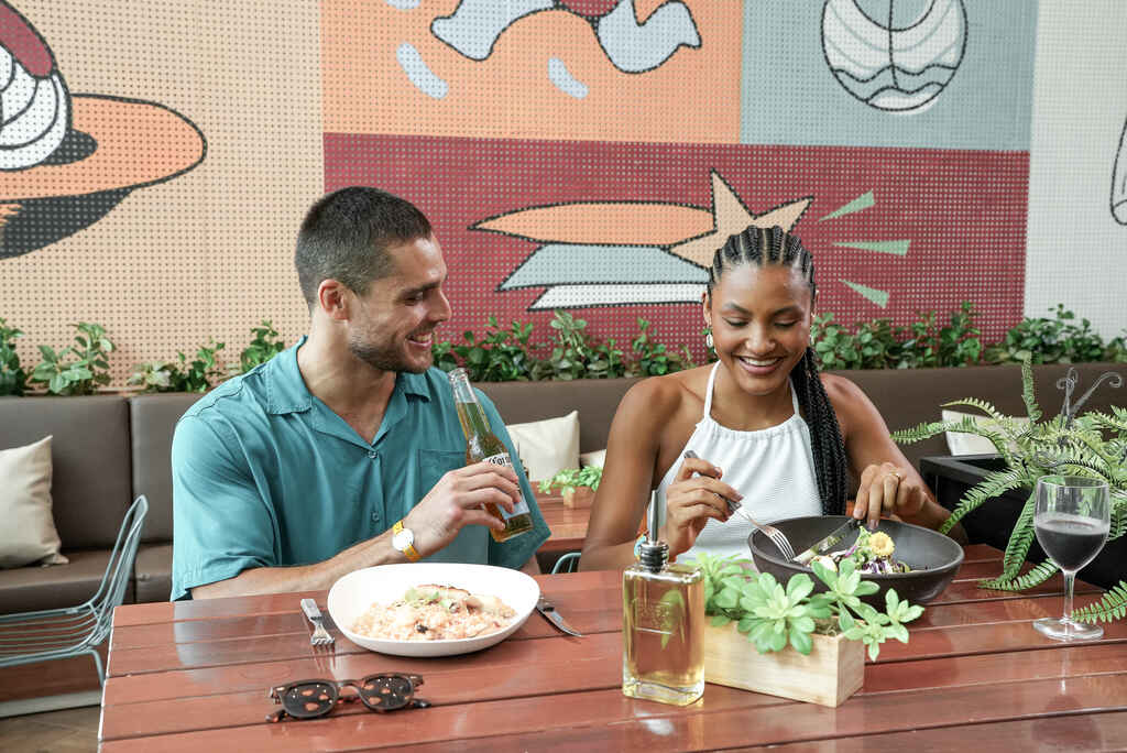 Casal aproveitando pratos de restaurante de resort, representando onde ir nas férias de julho.