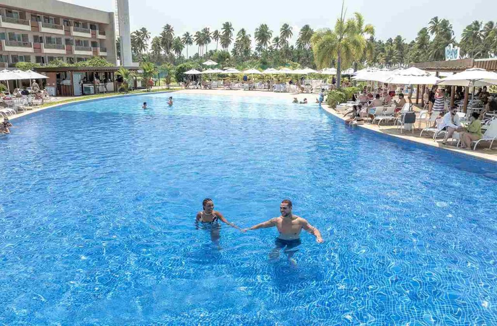 Duas pessoas em piscina de hotel, aproveitando viagem com tempo de qualidade.