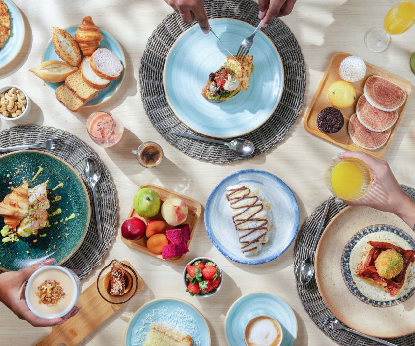 Mesa repleta de opções de café da manhã com frutas, pães, croissants, omeletes e sucos em um resort all inclusive premium.