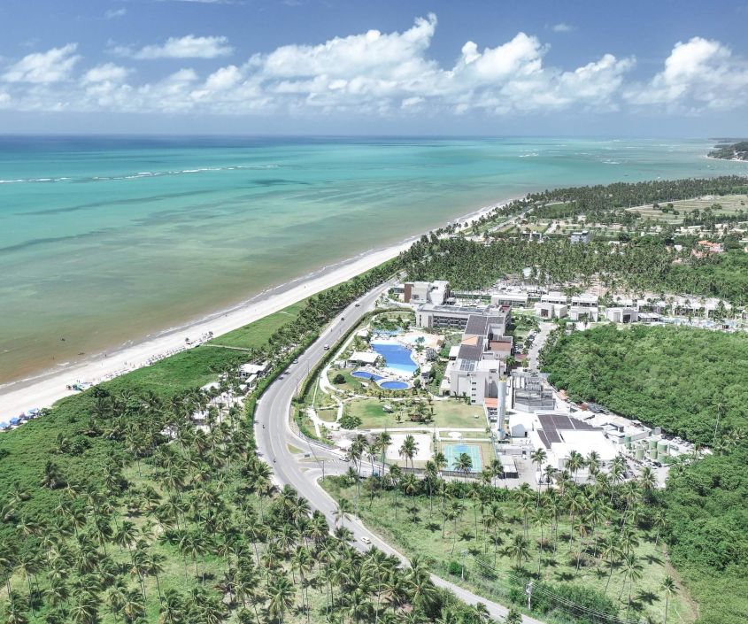 Vista aérea do Japaratinga Lounge Resort, com o mar azul ao fundo e áreas verdes ao redor.