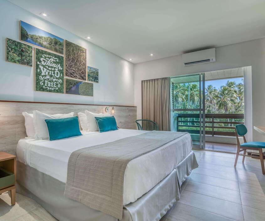 Apartamento Smart, com uma cama de casal, mesa para apoio, mesa de cabeceira, varanda com vista mangue e decoração em tons de verde.