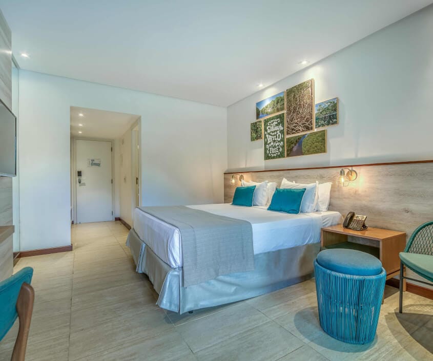 Apartamento Smart, com uma cama de casal, cadeira e puf, TV Smart, vista para entrada do quarto e decoração em tons de verde.
