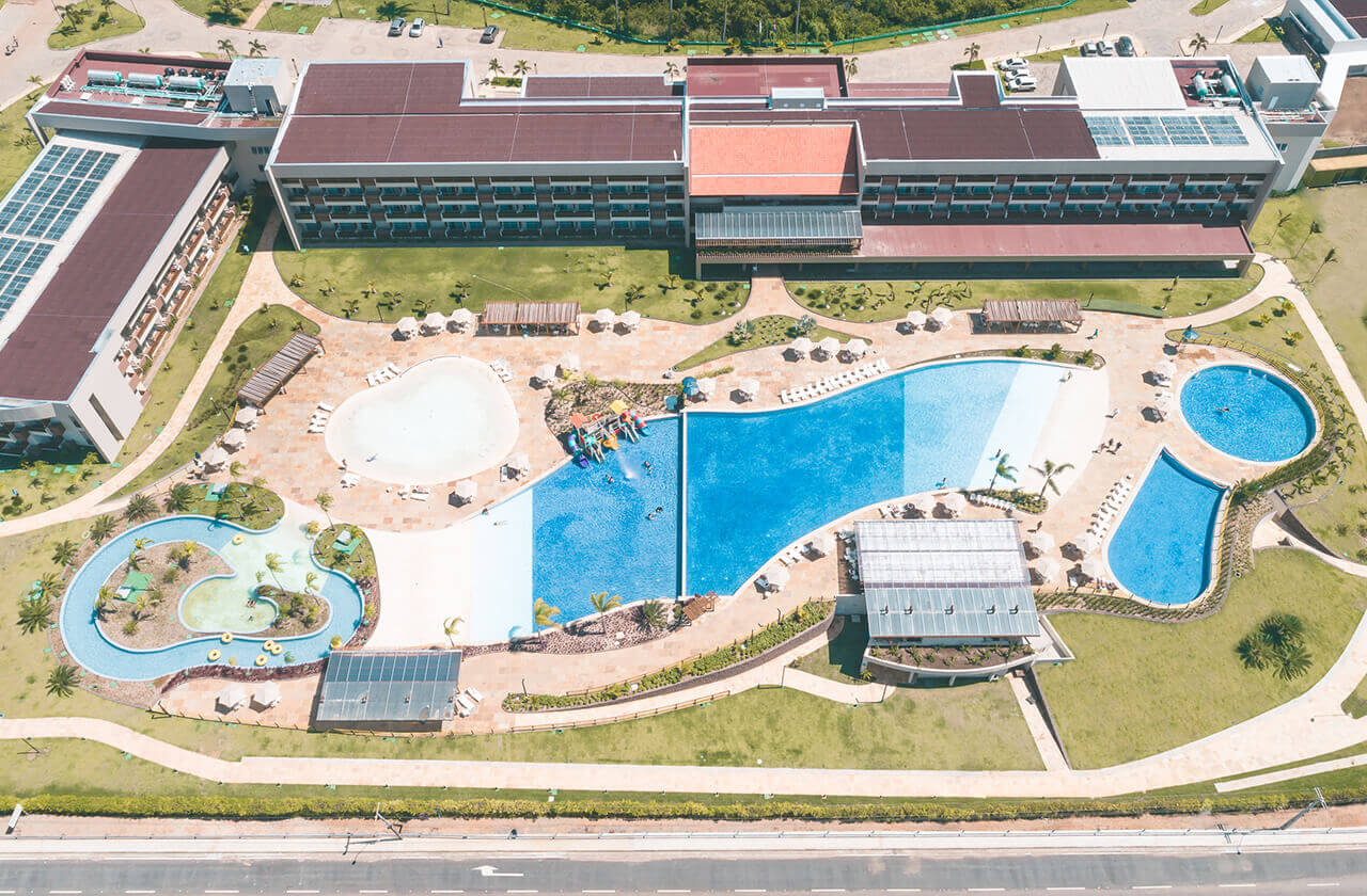 Vista aérea destacando o bloco de apartamentos e o complexo de piscinas do resort. A imagem mostra uma parte da infraestrutura do Japaratinga Lounge Resort.