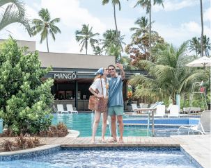 Casal tirando foto na ponte entre as piscinas do hotel. Ao fundo, o restaurante Mangô.