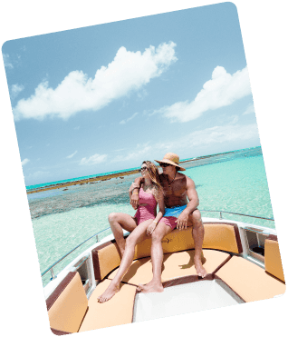 Casal curte passeio de barco nas piscinas naturais de japaratinga, céu com poucas nuvens. Ele está apenas de bermuda e um chapéu de palha e a mulher com maiô rosa e óculos escuros.