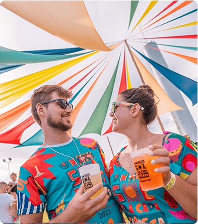 Casal segurando copo de cerveja sorri um para o outro durante o carnava no Japaratinga Lounge Resort