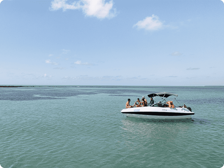 grupo de amigos na proa de uma lancha nas piscinas naturais de Japaratinga, o céu está com poucas nuvens.