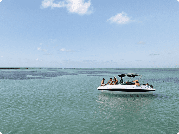grupo de amigos na proa de uma lancha nas piscinas naturais de Japaratinga, o céu está com poucas nuvens.