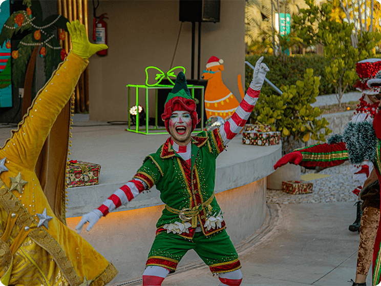 A Praça dos Coqueiros com o palco no fundo decorado com um telão digital de natal. E personagens natalinos fazendo uma apresentação.