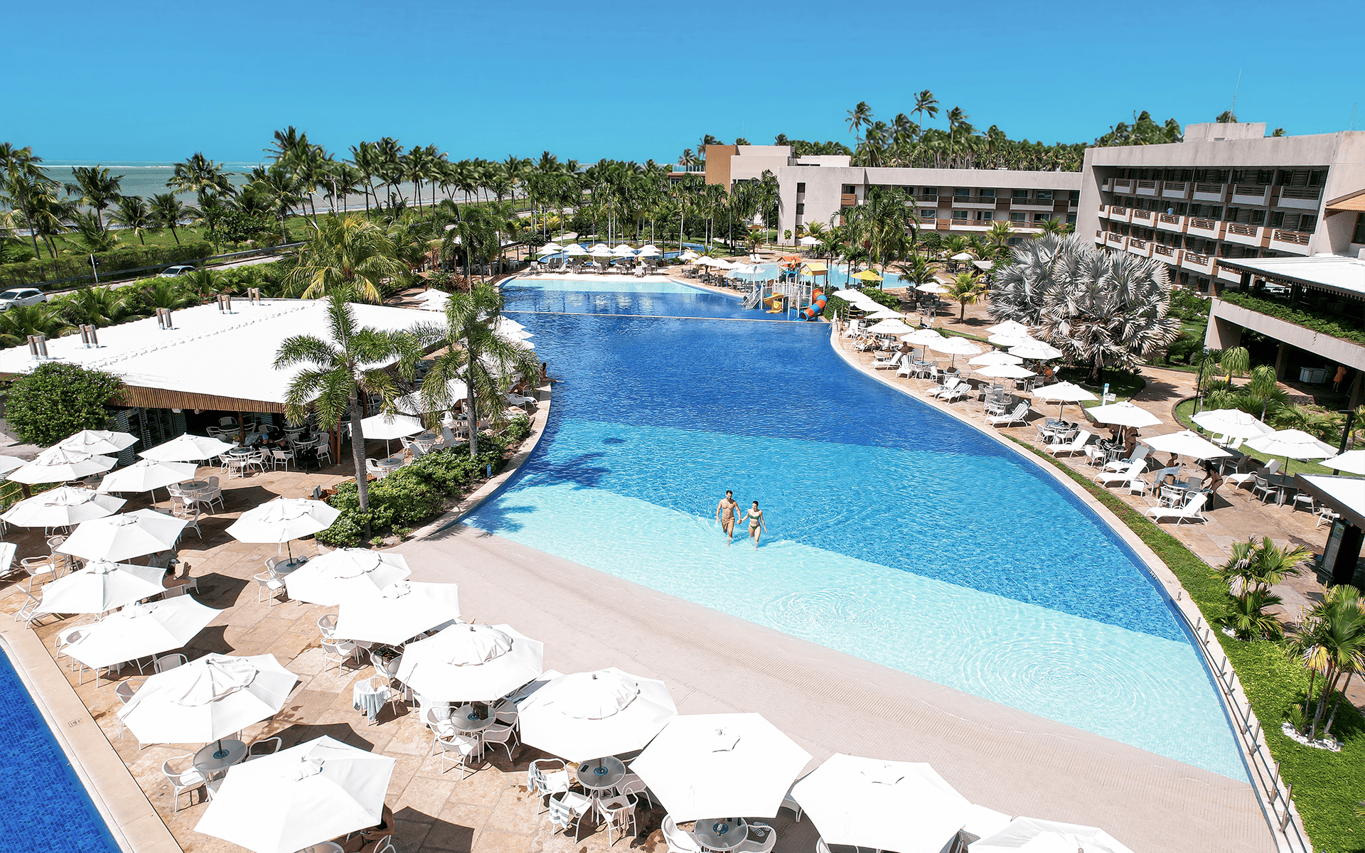 Piscina principal do do Japaratinga Lounge Resort com  borda infinita e simulação de praia na parte rasa com vista para a área de lazer.