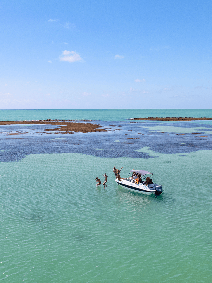 Piscinas naturais de Japaratinga com águas cristalinas e recifes com lancha ancorada no mar.