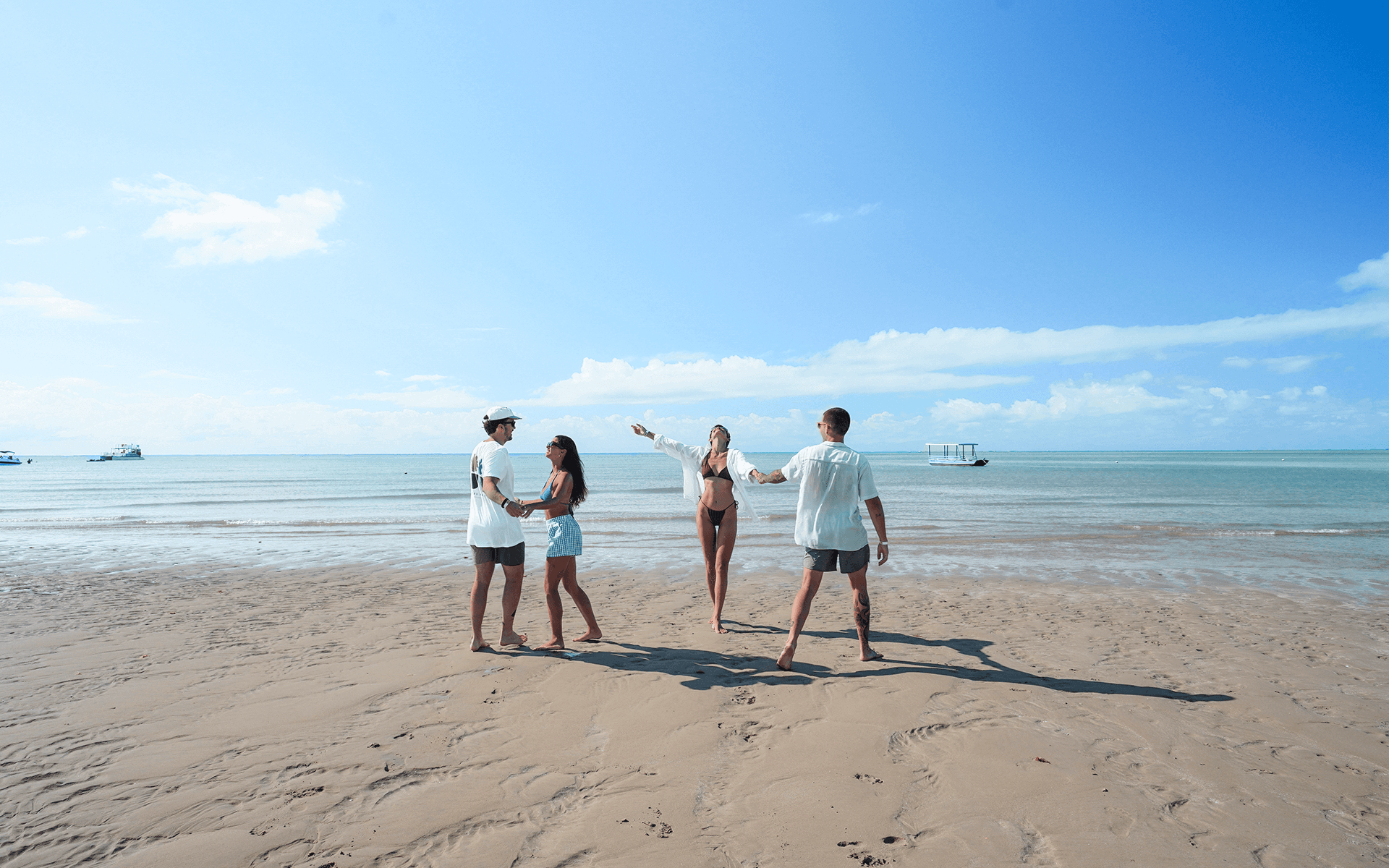 Grupo de amigos caminhando e se divertindo na faixa de areia da praia de Japaratinga durante o dia ensolarado.