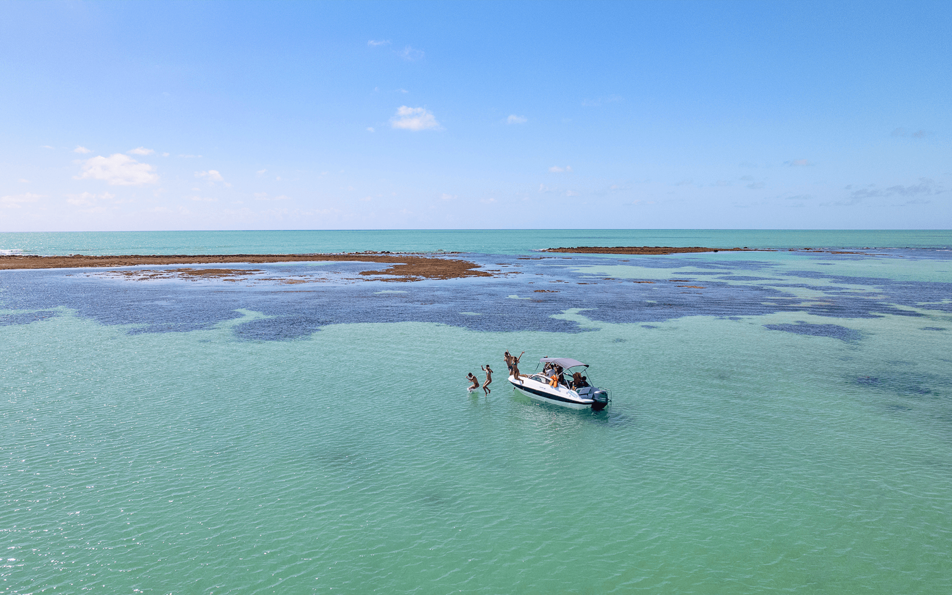 Piscinas naturais de Japaratinga com águas cristalinas e recifes com lancha ancorada no mar.