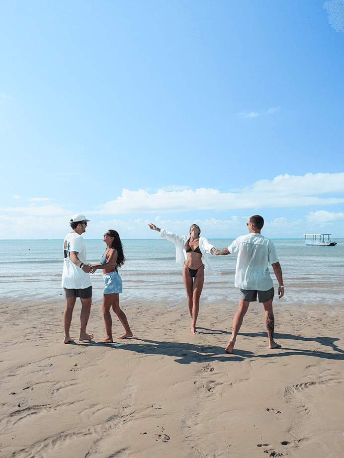 Grupo de amigos caminhando e se divertindo na faixa de areia da praia de Japaratinga durante o dia ensolarado.