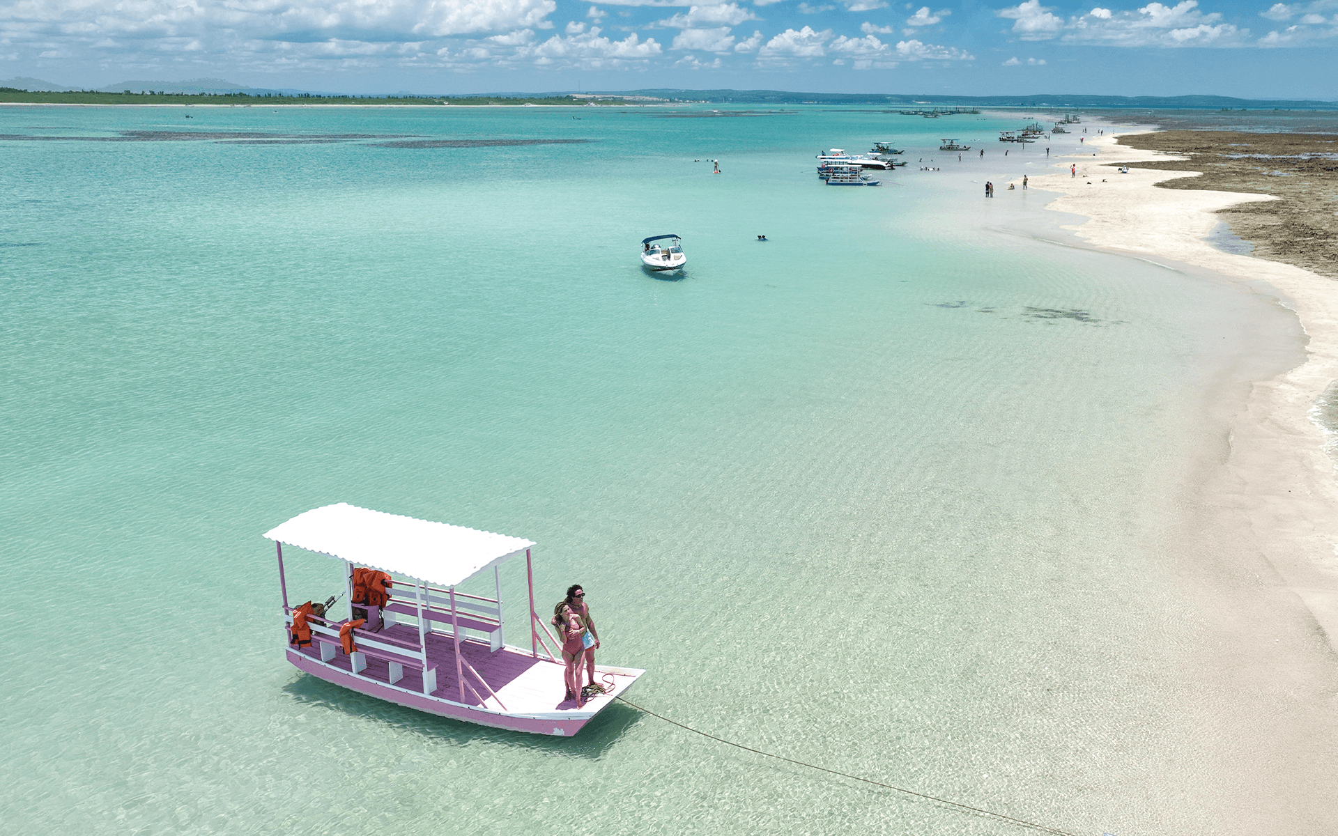 Passeio de jangada ancorada em águas cristalinas das piscinas naturais da praia de Japaratinga. Possível ver os recifes de corais e casal em cima da jangada rosa.