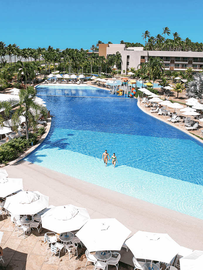 Piscina principal do do Japaratinga Lounge Resort com  borda infinita e simulação de praia na parte rasa com vista para a área de lazer.