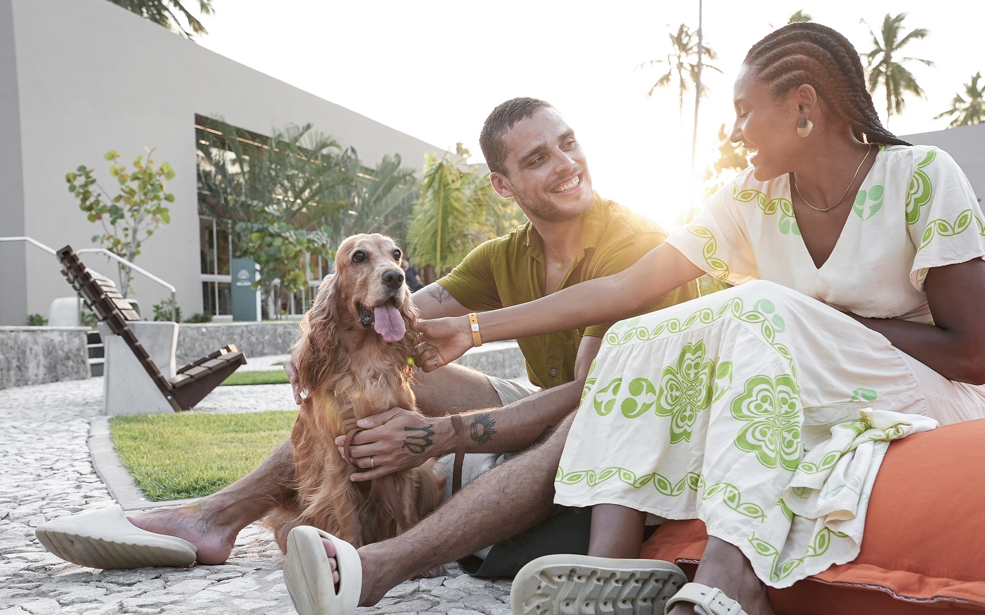 dog-friendly-japaratinga-lounge-resort Casal com cachorro curtindo área da Praça dos coqueiros ao pôr do sol no Japaratinga Lounge Resort, em ambiente dog friendly com coqueiros ao fundo.