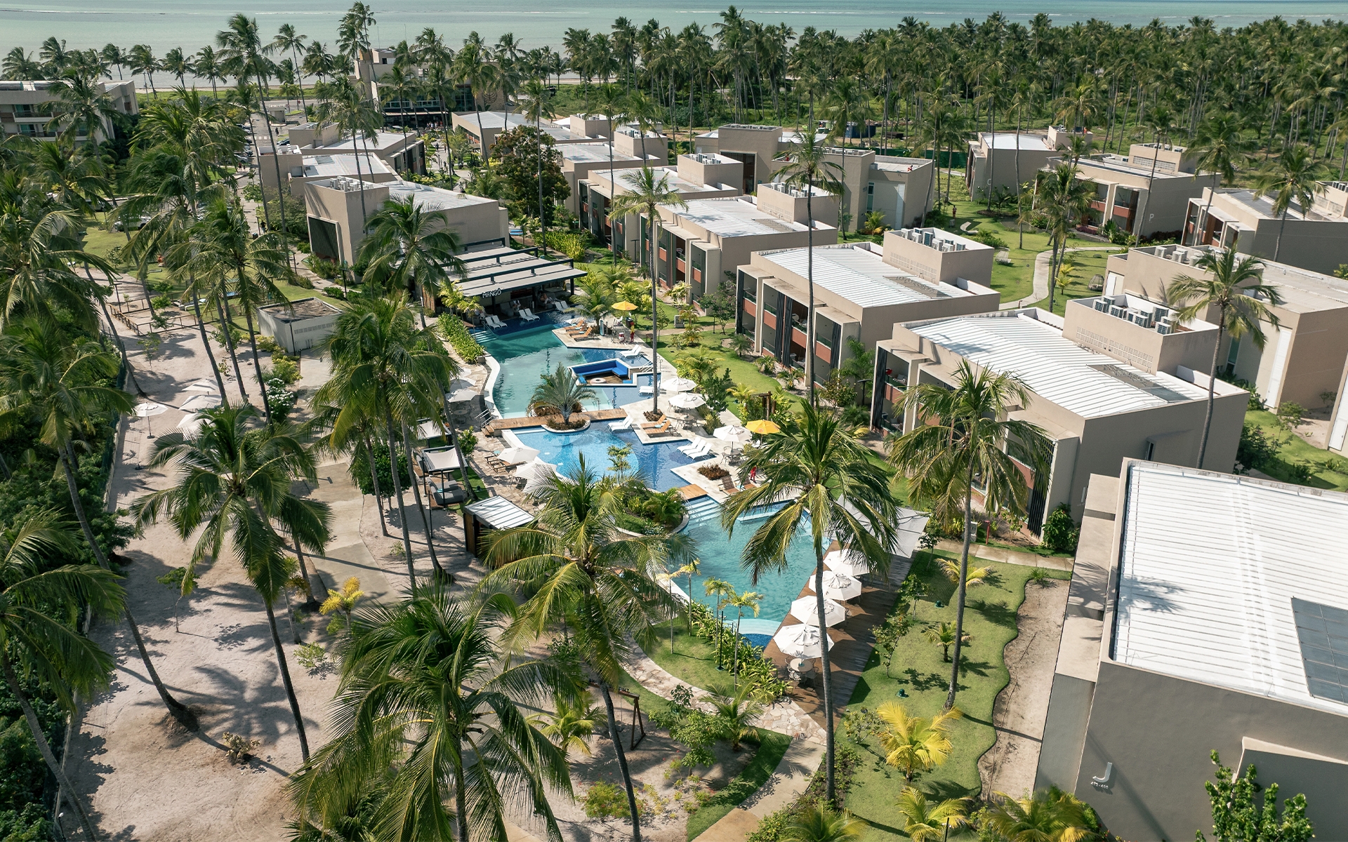 apartamentos-gardens Vista aérea dos novos apartamentos Garden do Japaratinga Lounge Resort, com piscina em formato orgânico, coqueiros e jardins integrados ao paraíso natural. E ao fundo o Mangô Bar.