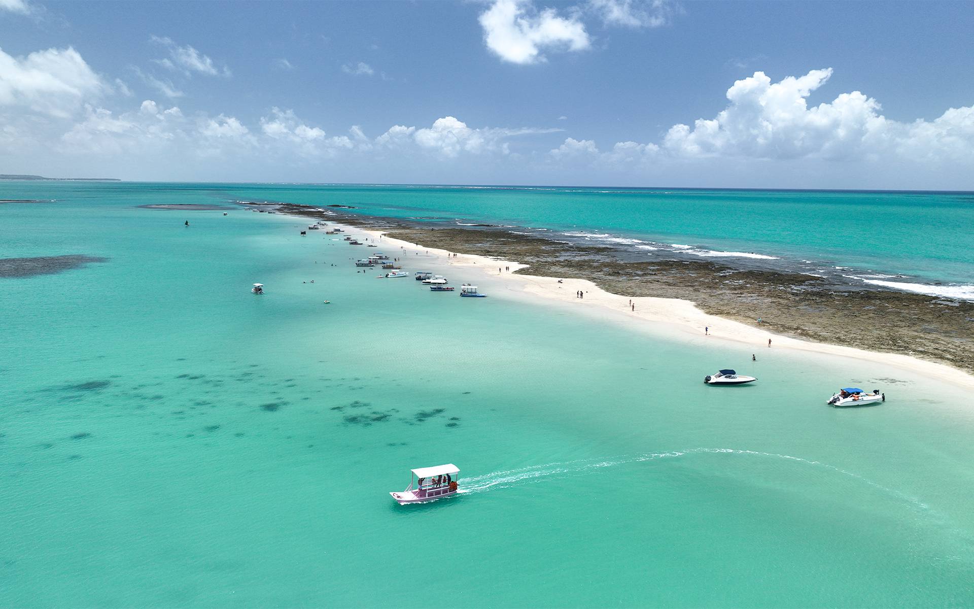 Vista aérea da Croa de São Bento em Maragogi, com bancos de areia, águas cristalinas azul-turquesa e barcos ancorados