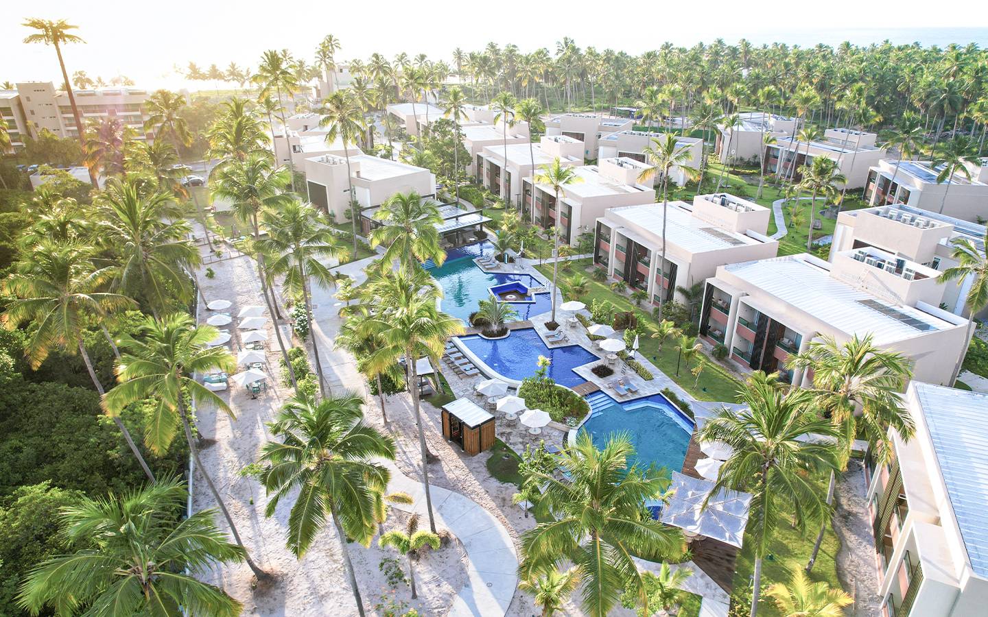 Vista panorâmica da área de piscinas do Bar Mangô do Japaratinga Lounge Resort, mostrando as Gardens com varandas, coqueirais e espreguiçadeiras à beira da piscina.