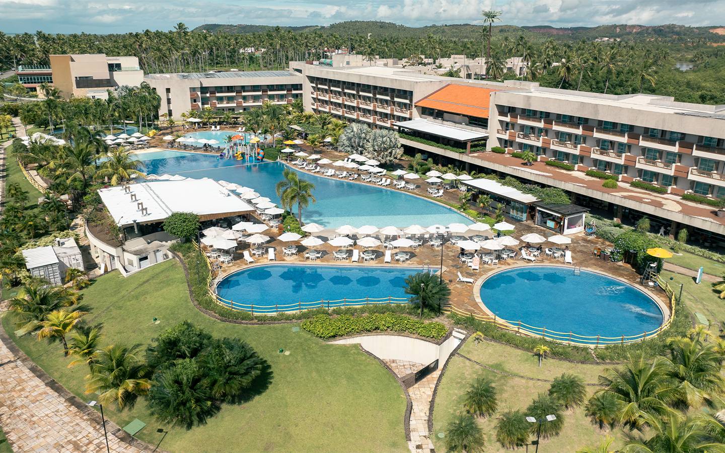 Vista aérea do Japaratinga Lounge Resort à beira-mar, com piscinas amplas e quadras, cercado por vegetação e coqueiros. E no canto esquerdo um é possível ver a praia de Japaratinga.