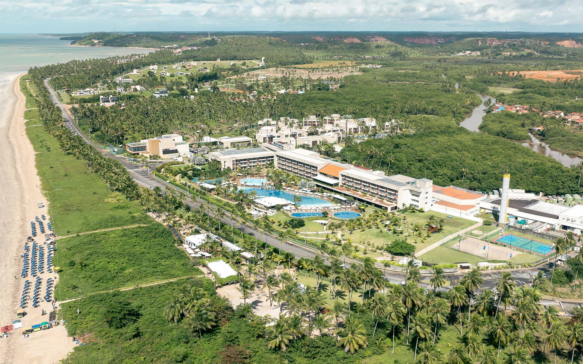 Vista aérea do Japaratinga Lounge Resort à beira-mar, com piscinas amplas, cercado por vegetação e coqueiros. E no canto esquerdo um é possível ver a praia de Japaratinga.