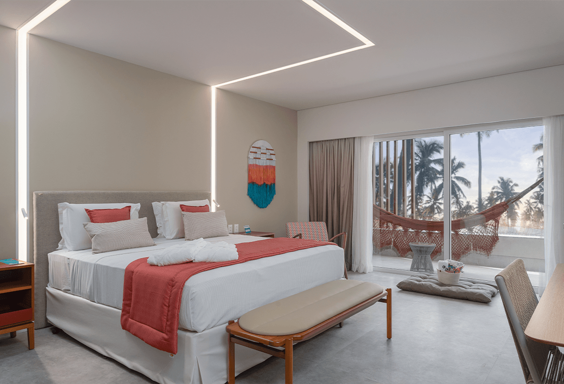 Apartamento Garden Exclusive com grande cama no centro, ao fundo a varanda pra área externa com rede pendurada.