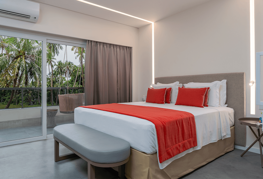 Garden Suite com detalhes das áreas da acomodação, com cama ao centro do quarto, vista pra área externa, que comporta até quatro ocupantes.