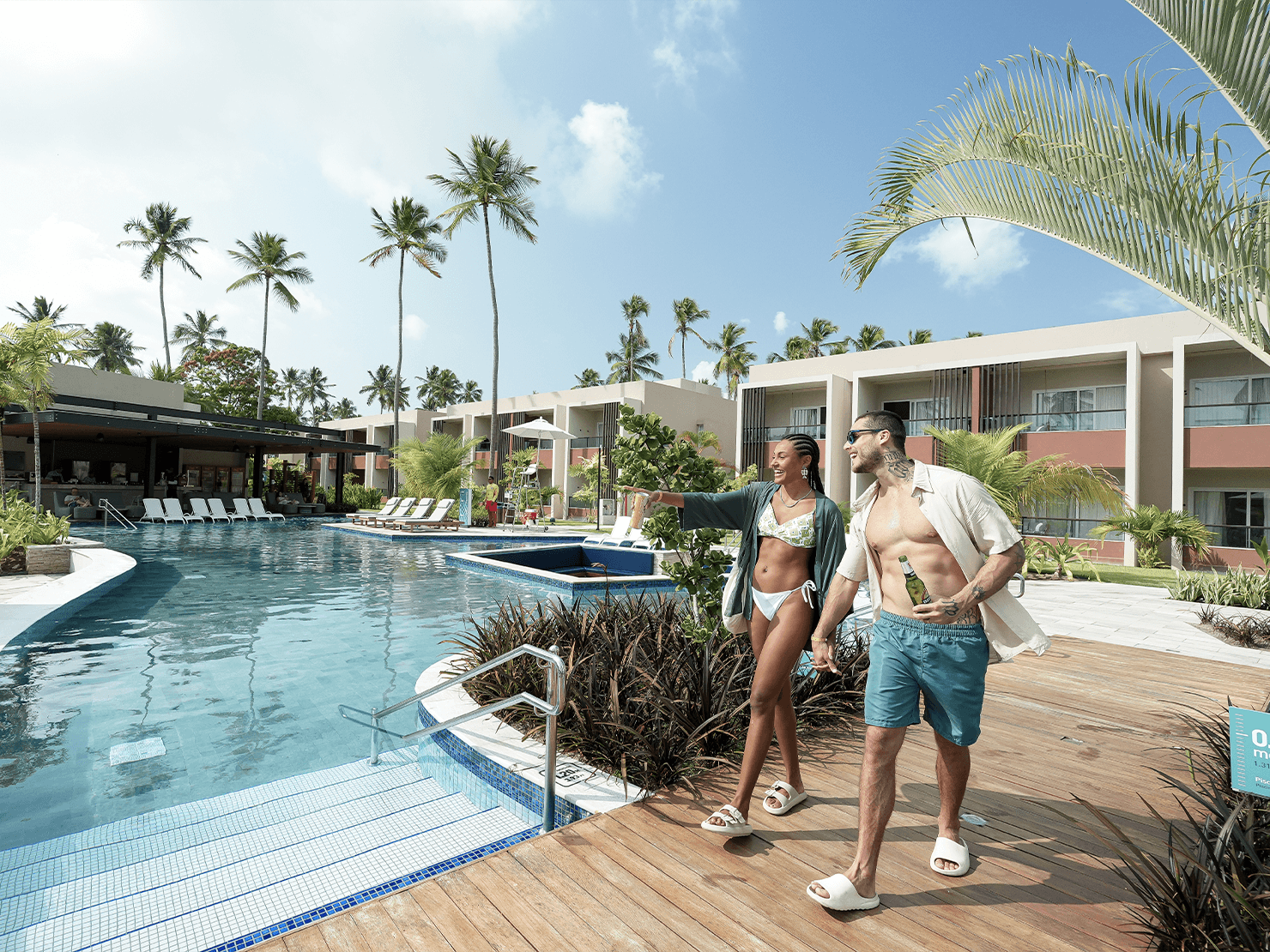Casal caminhando de mãos dadas na área da piscina das Gardens no Japaratinga Lounge Resort, em cenário paradisíaco com coqueiros e estrutura moderna All Inclusive Premium.