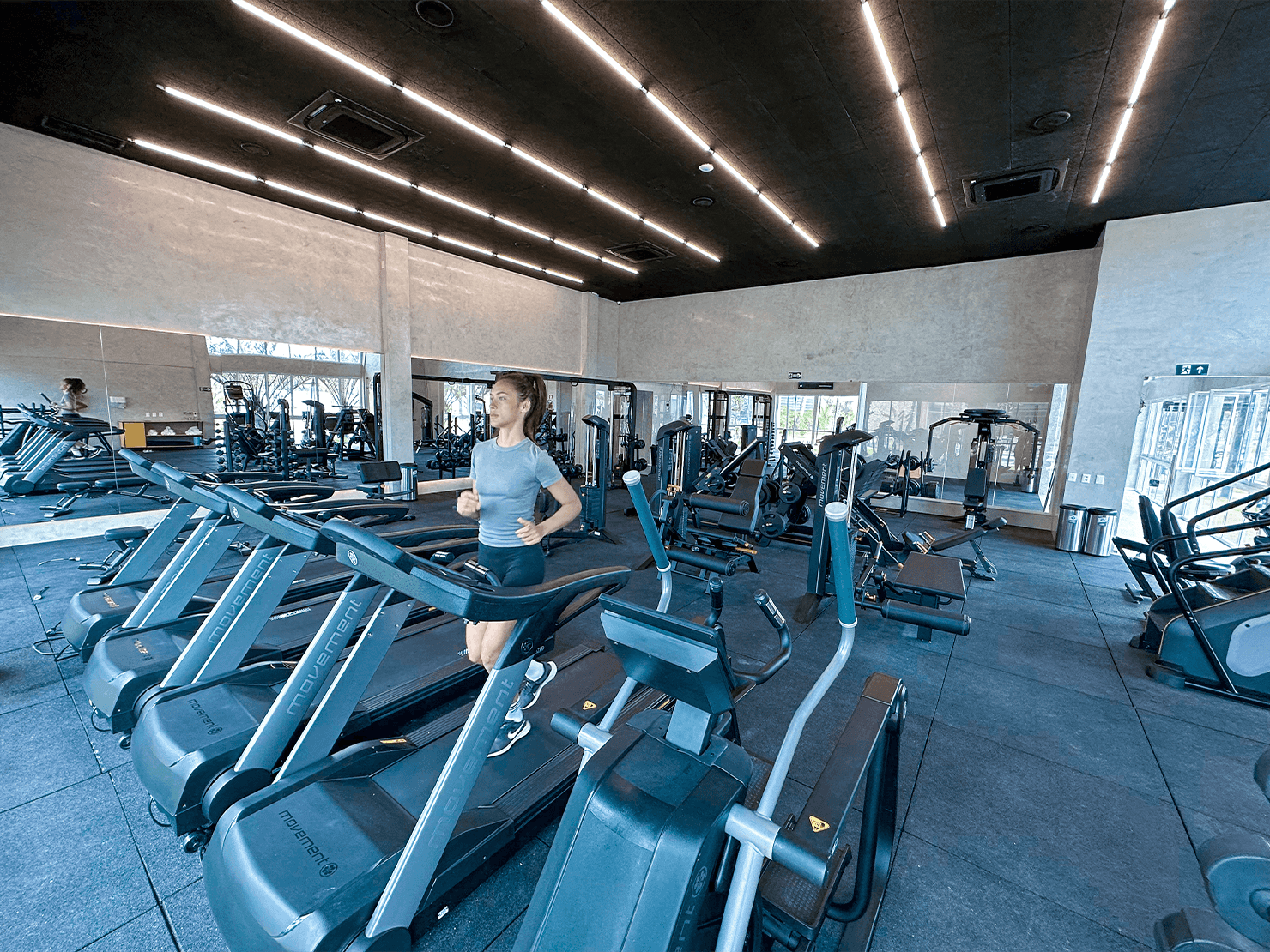 Hóspede praticando corrida em esteira no Espaço Wellness do Japaratinga Lounge Resort. Ambiente com design industrial, iluminação linear e equipamentos de alta performance.